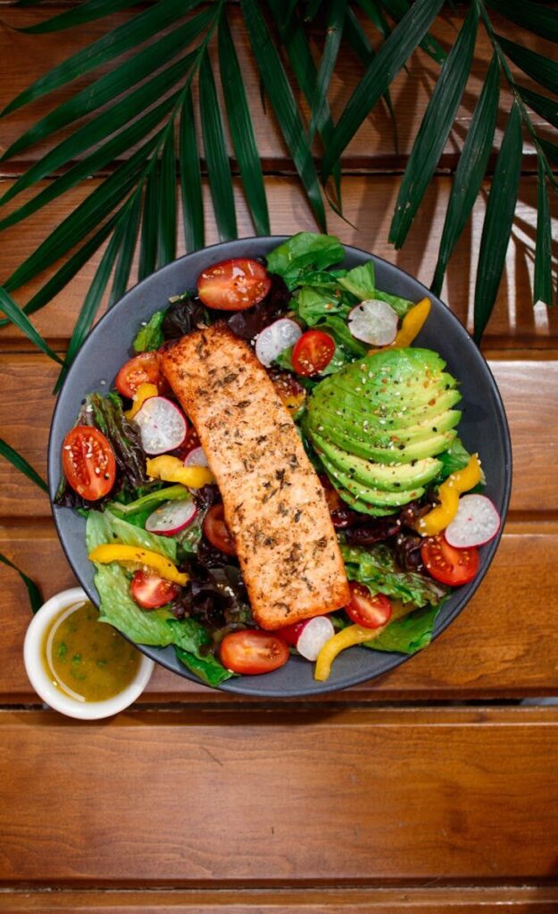 Delicious garden salad featuring grilled salmon, avocado, and fresh vegetables on a wooden surface.