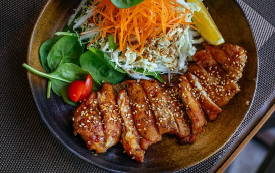 A savory chicken salad bowl garnished with sesame seeds, fresh vegetables, and lemon wedge.