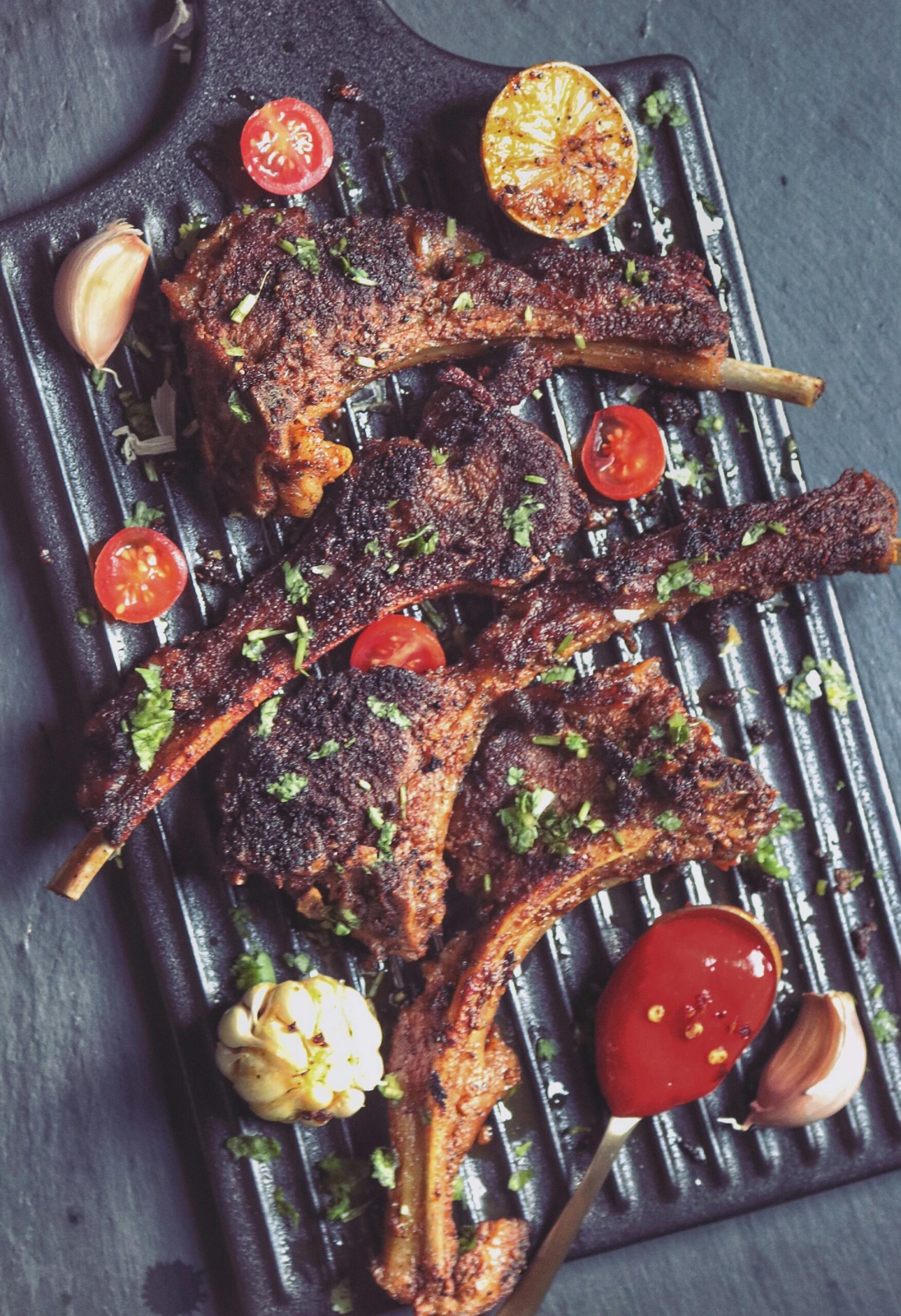 Delicious grilled lamb chops sprinkled with herbs and served with garlic, cherry tomatoes, and sauce.