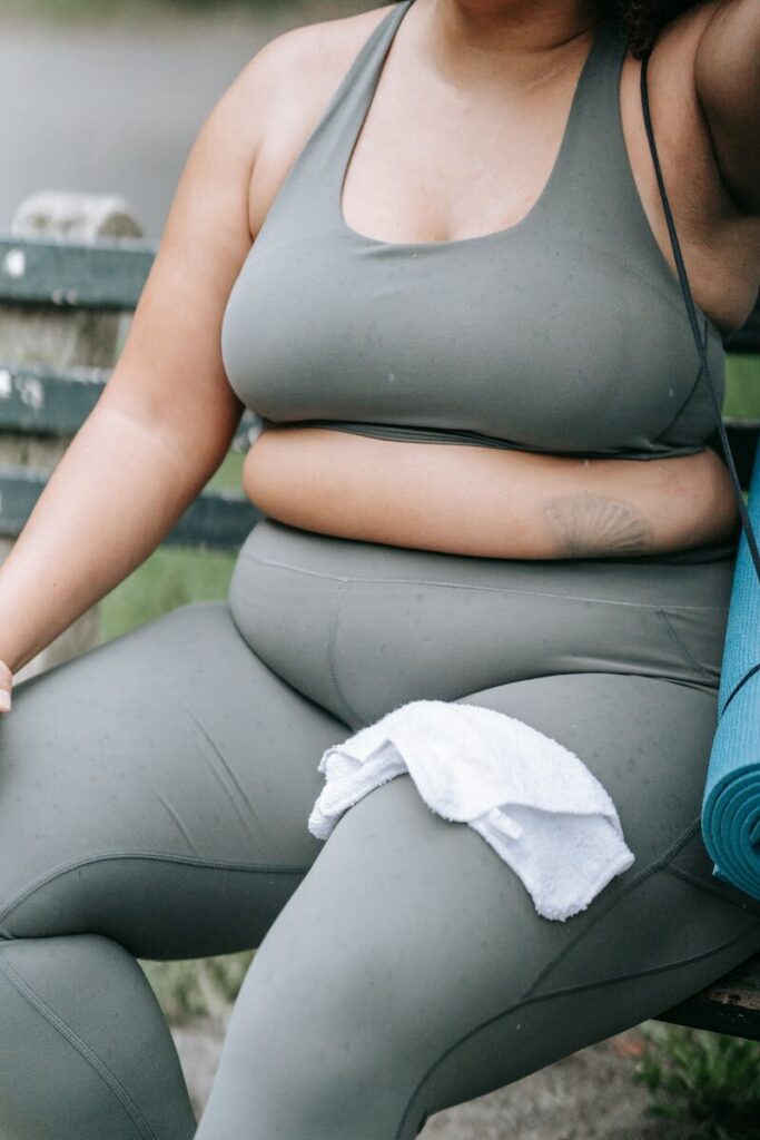 Plus-size woman resting with yoga mat and towel in sports attire, embodying confidence.