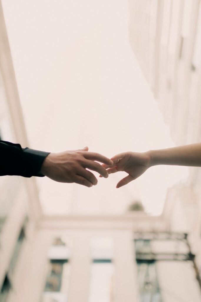 A romantic scene of two hands reaching towards each other in an outdoor urban setting.