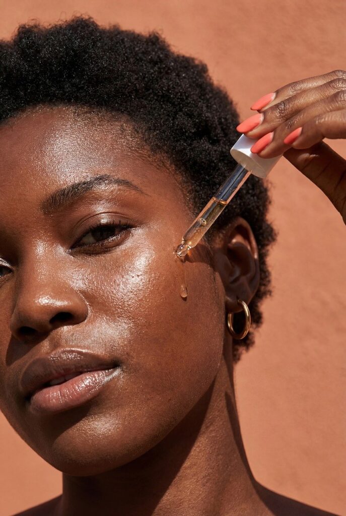 skincare, beauty, serum, face, woman, glowing, skin, oil, dropper, health, radiant, wellness, self-care, cosmetics, facial, moisturizer, natural, routine, luxury, portrait, black woman, orange, terracotta, sun-kissed, hydration