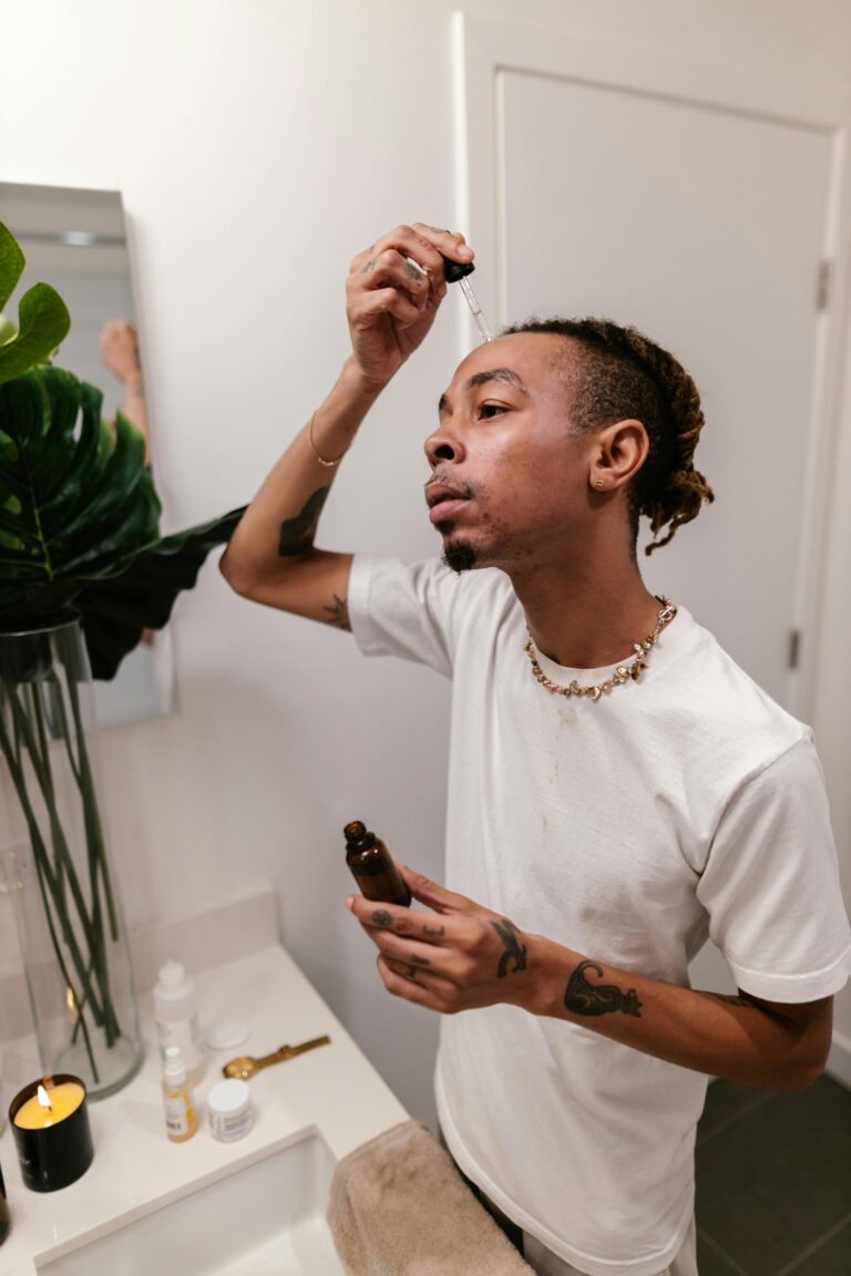 A man applies skincare serum using a dropper in a modern bathroom setting.